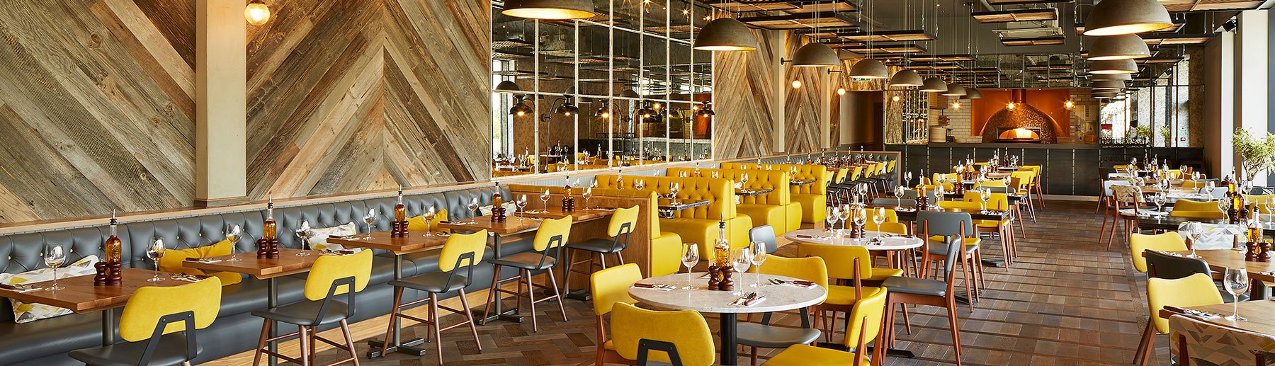 Wildwood Telford interior: Vibrant yellow chairs accentuate the space, with the pizza oven visible in the background