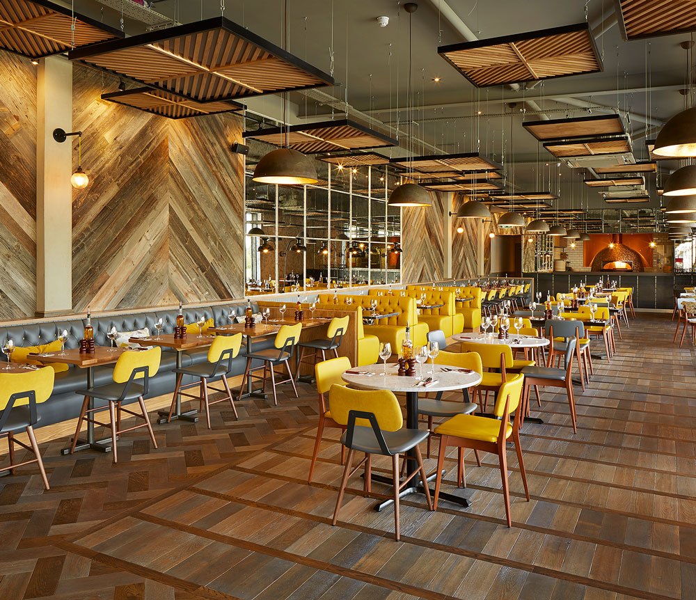 Inside Wildwood Telford: yellow chairs add a pop of color, with a glimpse of the pizza oven in the distance